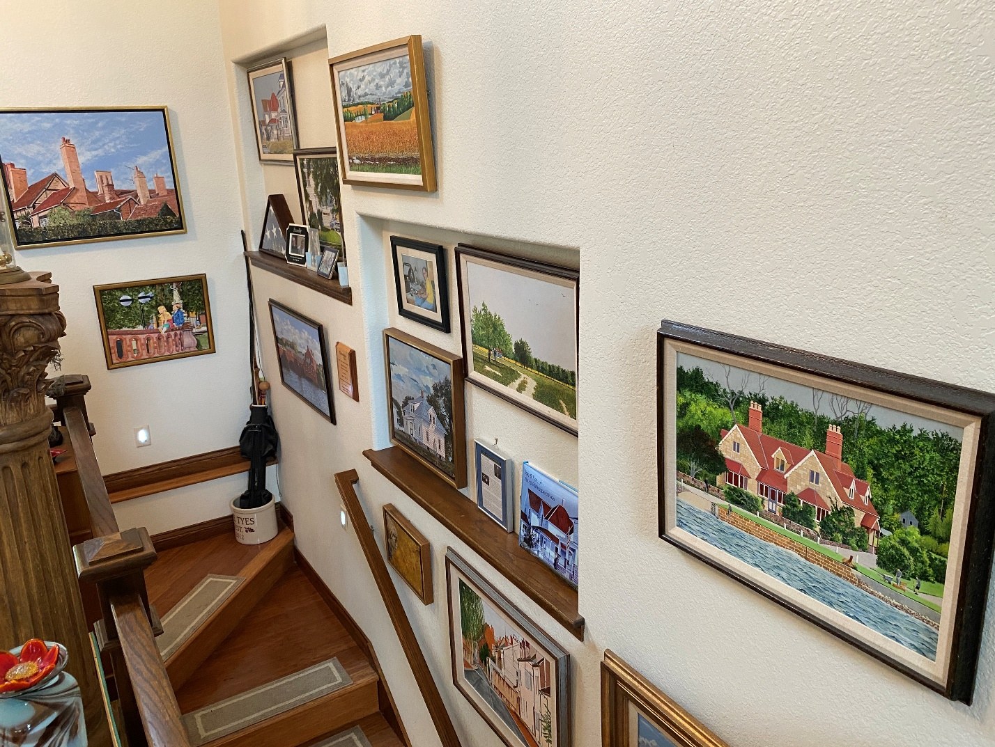 A stairway wall displaying a collection of framed original paintings